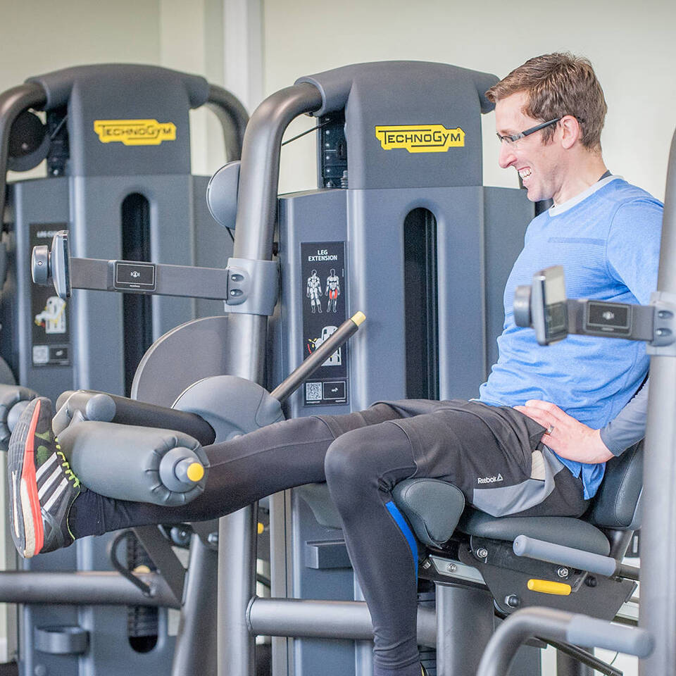 A male using a leg extension resistance machine at Woodbury Park's gym
